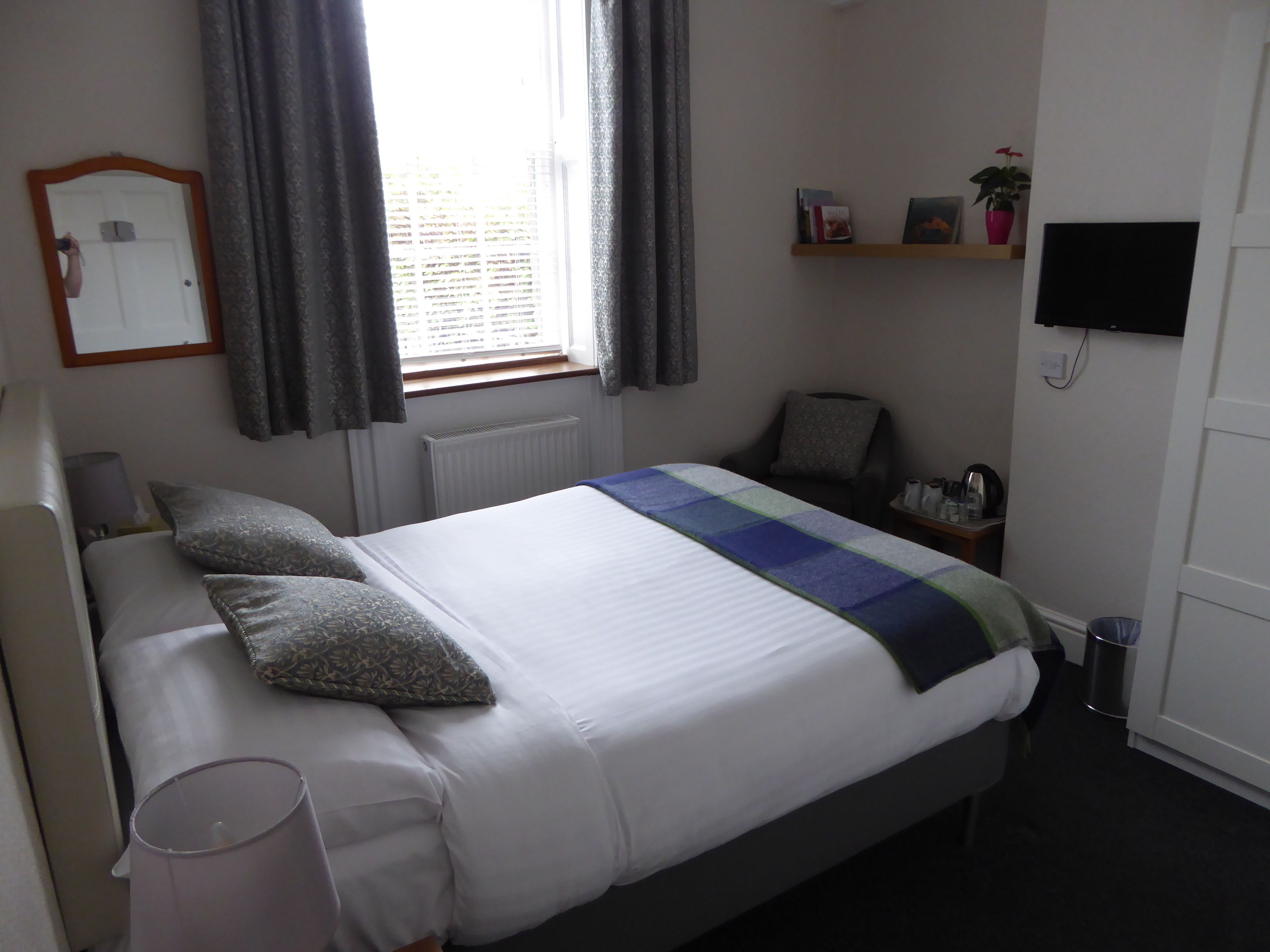 A neatly arranged hotel room with a bed, bedside lamp, and a television mounted on the wall.