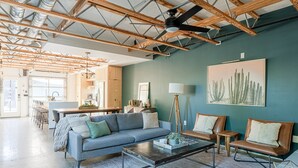 Un amplio salón con un sofá, una mesita de centro y dos sillones. Un cuadro de cactus cuelga de la pared, y hay un ventilador de techo.