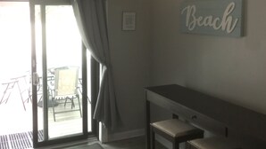 A room with a ceiling fan, a sliding glass door leading to an outdoor area, a small table with a chair, and a wall-mounted sign that reads "Beach". - BEST BRIGANTINE VALUE! WE PAY BEACH FEES. WALK TO BEACH, EATERIES. 11AM CHECKOUT (Brigantine)