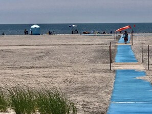 Ein Strand mit einer blauen Weges, der zum Wasser führt, Sonnenschirmen und Badegästen.