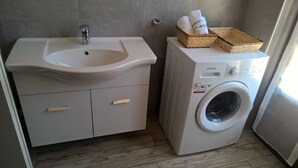 A bathroom with a sink, a washing machine, and a basket with towels. - Villa Sofia Piedmont  (Montaldo Scarampi)
