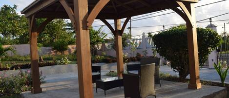 A wooden pergola with a table and chairs in a garden setting.