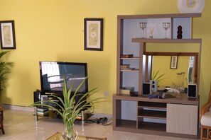 Una sala de estar con televisor, mueble de madera para entretenimiento y una planta en maceta.