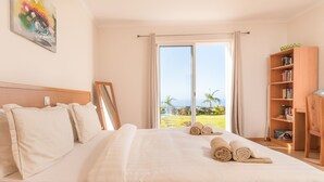 A hotel room with a large bed, a bookshelf, and a view of the ocean. - SUN AND SUN HOUSE (Arco da Calheta)