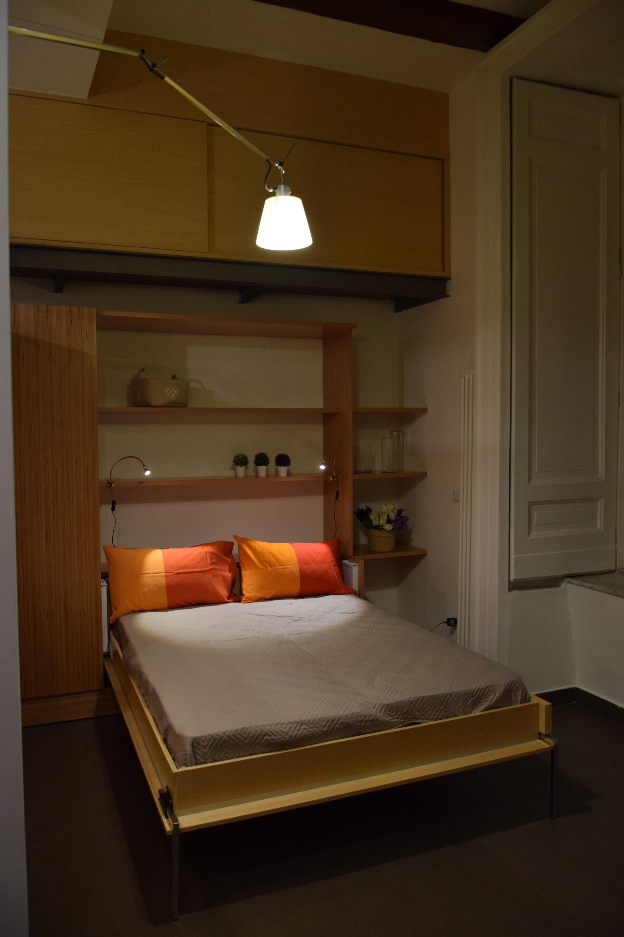 Une chambre compacte comprenant un lit, des étagères intégrées et un espace bureau.