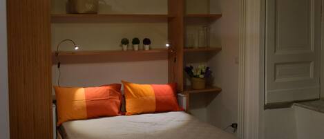 Une chambre compacte comprenant un lit, des étagères intégrées et un espace bureau.