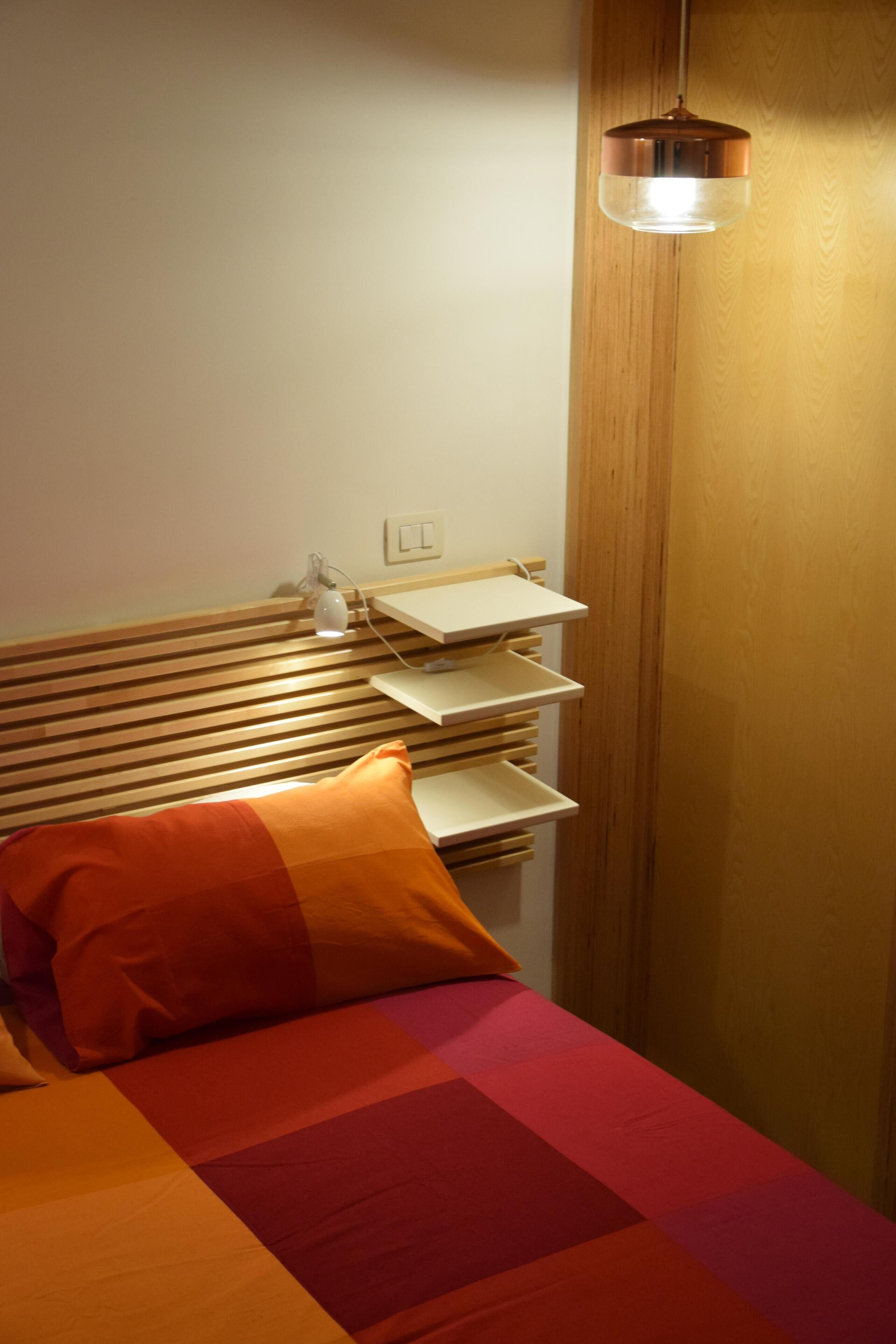 A neatly made bed with a striped headboard, a bedside table with a lamp, and a wooden wardrobe.