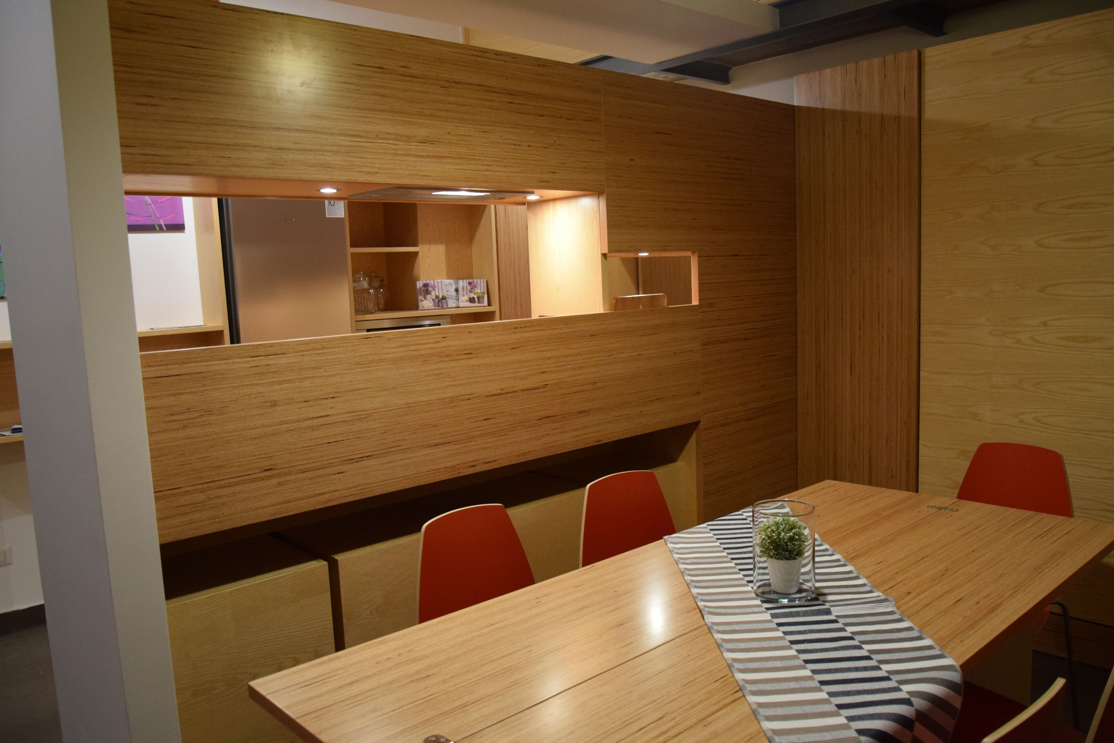 A conference room with a long wooden table, red chairs, and a patterned table runner.