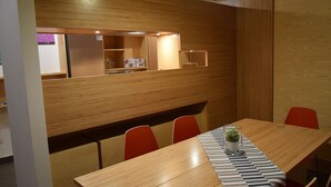 Uma sala de conferências com uma longa mesa de madeira, cadeiras vermelhas e um jogo americano estampado.