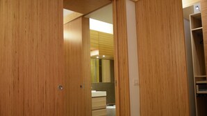Quarto moderno com guarda-roupas de madeira, cama vermelha e banheiro com espelho e pia.