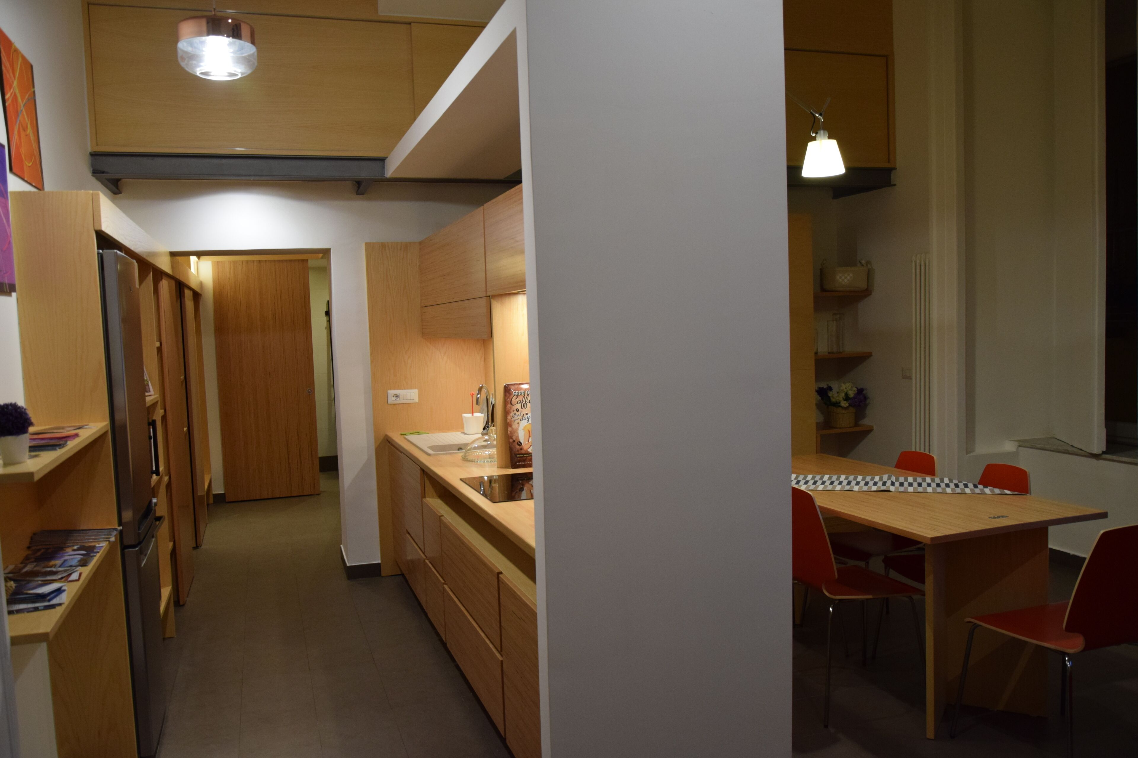 Una cocina moderna con armarios de madera, una mesa de comedor con sillas rojas y un ventanal pequeño.