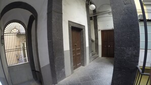 Um corredor com colunas de pedra, uma porta de madeira e uma janela com grades.