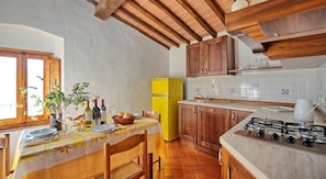 Una cocina con armarios de madera, un refrigerador amarillo, una mesa de comedor con platos y vasos, y una estufa a gas.