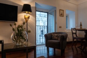 A living room with a sofa, a glass table with a vase, a floor lamp, and a view of the outside through a glass door. - Stunning Pantheon View experience in the heart of Rome (Roma)