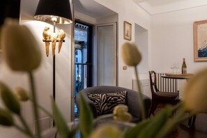 A cozy living room with a modern lamp, a comfortable sofa, a dining table with chairs, and a view of the outside.