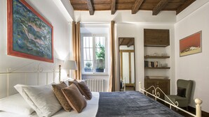 A bedroom with a bed, a window with curtains, a radiator, a bookshelf, and a painting on the wall. - Stunning Pantheon View experience in the heart of Rome (Roma)
