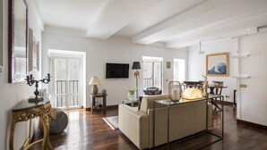 A spacious living room with a sofa, a dining table, and a TV mounted on the wall. - Stunning Pantheon View experience in the heart of Rome (Roma)