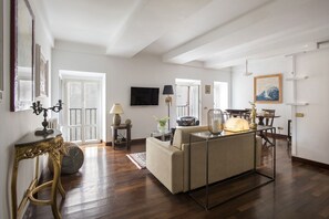 A spacious living room with a sofa, a dining table, and a TV mounted on the wall.
