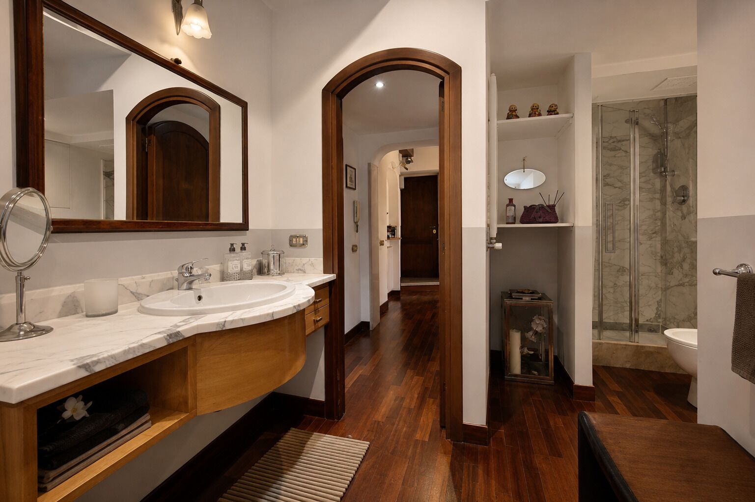 A bathroom with a marble sink, wooden vanity, and a glass shower enclosure.