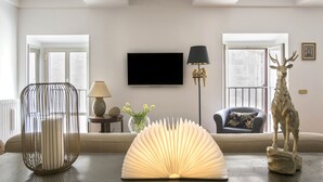 A living room with a sofa, a lamp, a decorative sculpture, and a flat-screen TV mounted on the wall. - Stunning Pantheon View experience in the heart of Rome (Roma)