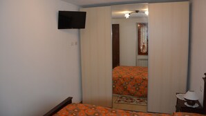 A bedroom with a bed, a television mounted on the wall, a wardrobe, and a mirror reflecting the room.