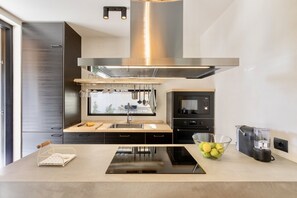 A modern kitchen with a stainless steel range hood, a built-in oven, a coffee maker, and a bowl of lemons on the counter.