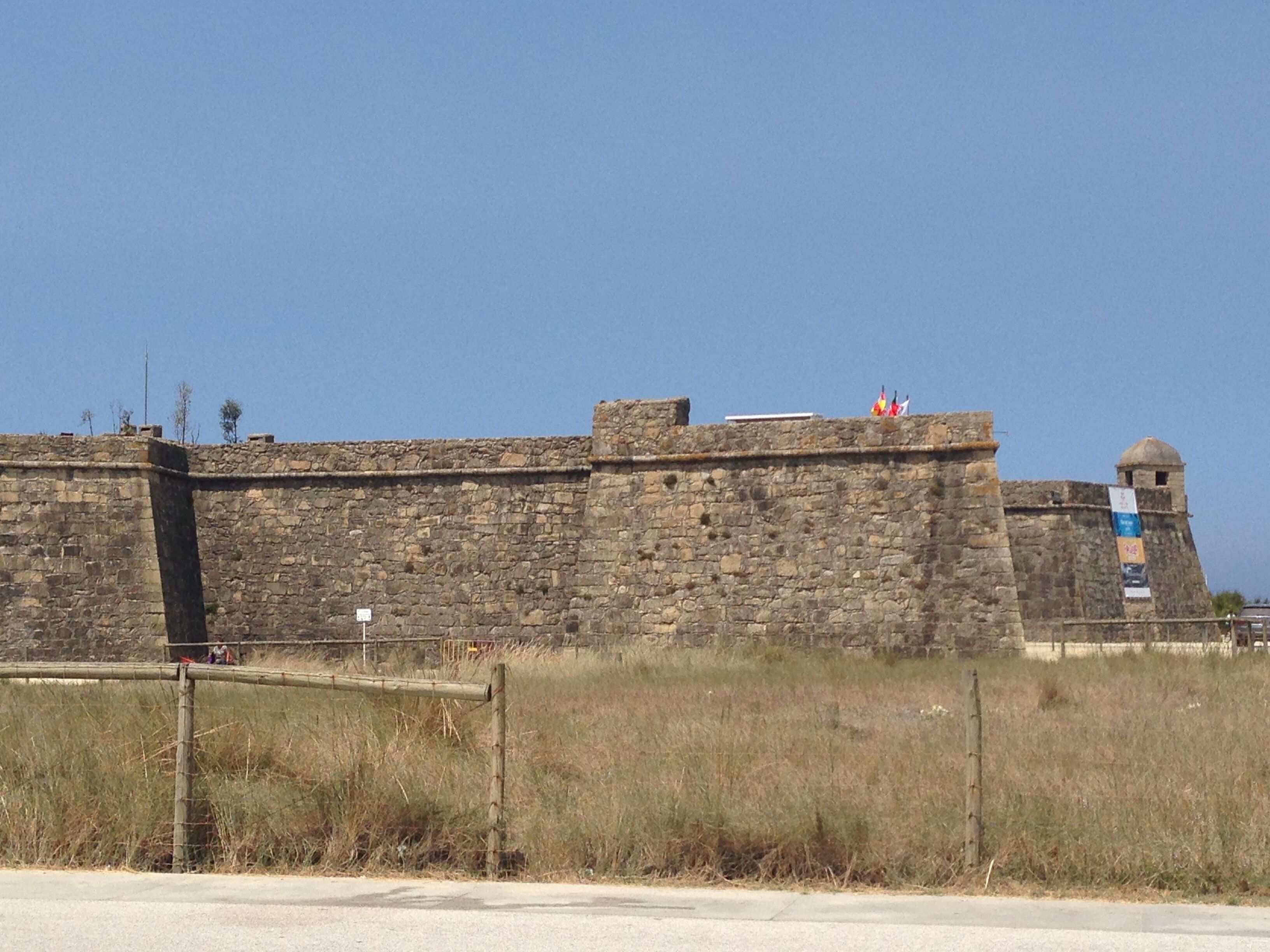 Una fortificazione in pietra con una torre di guardia, una bandiera e uno stendardo.