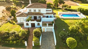 Una amplia casa de dos plantas con piscina, rodeada de céspedes y jardines bien cuidados.