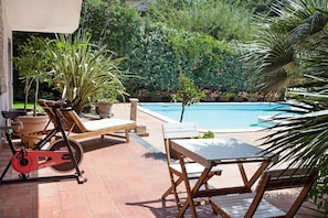 Un espace extérieur avec une piscine, un vélo d’exercice fixe, des chaises longues et une table.