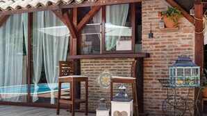 Una mesa y sillas de madera frente a un edificio con pared de ladrillo y grandes ventanales.