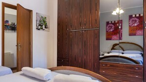 Una habitación de hotel con un armario de madera, una cama con ropa blanca y un espejo que refleja el espacio.