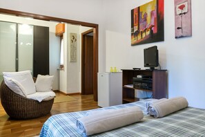 Une chambre à coucher avec un lit, un fauteuil en osier avec des coussins, une télévision et des œuvres d’art accrochées au mur.