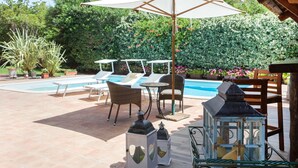Un área junto a la piscina con sillones de descanso, una mesa y un farol.