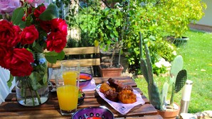 Une table en bois sur laquelle se trouvent un vase de roses rouges, un verre de jus d’orange, une assiette de muffins et un cactus.