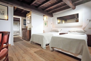 A room with two beds, wooden flooring, a wooden ceiling, and framed artwork on the walls.