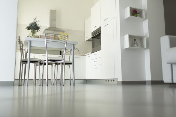 Une cuisine moderne avec des meubles blancs, une table à manger avec des chaises et un vase rempli de fleurs.