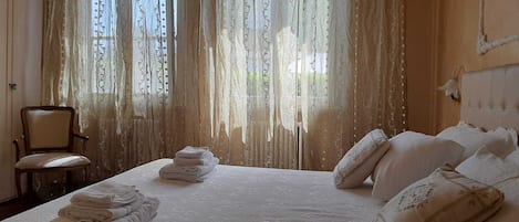 A neatly made bed with folded towels, a chair, and a window with curtains.