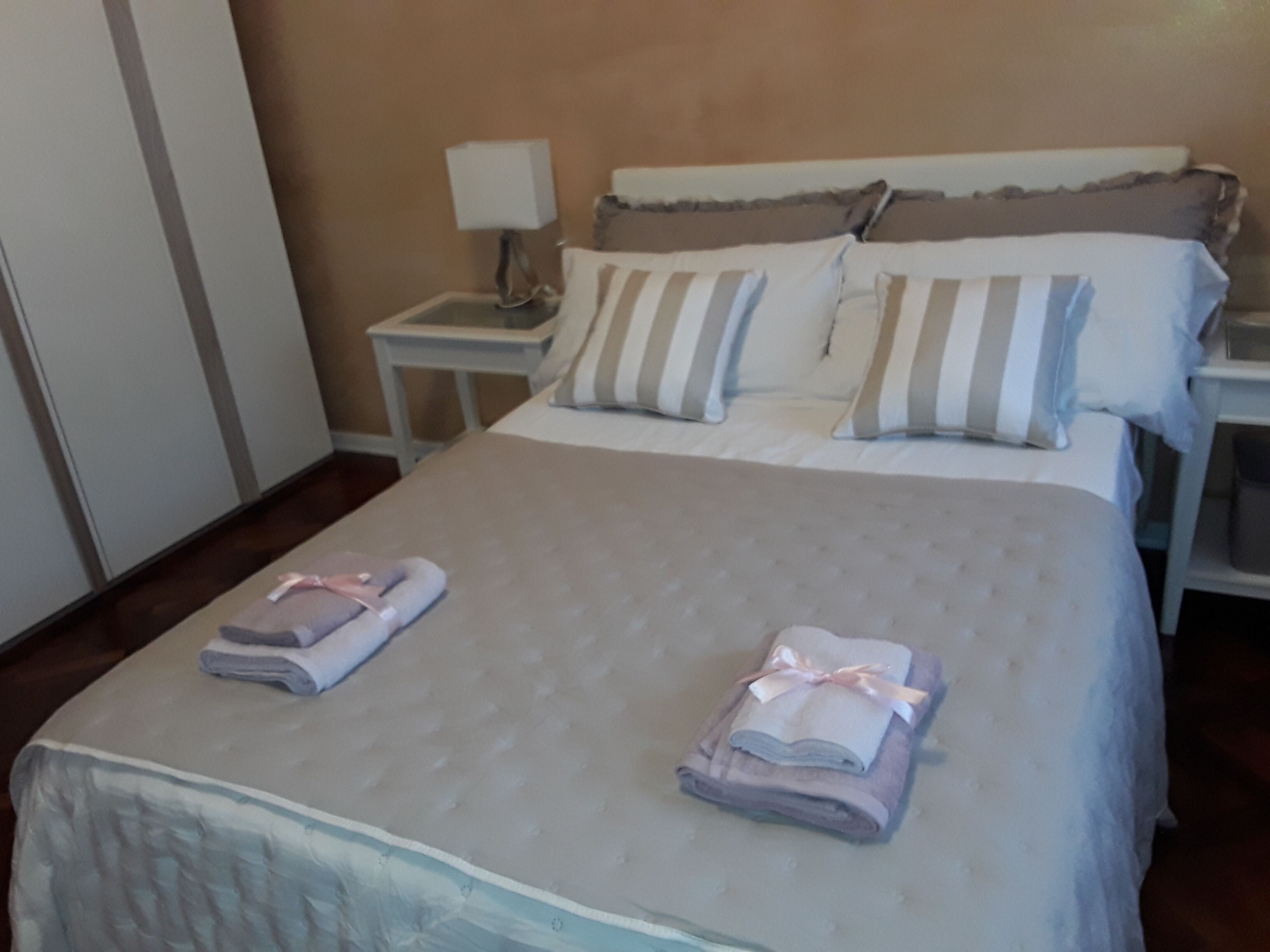 Una cama bien hecha con almohadas a rayas, una lámpara de noche y toallas dobladas sobre la cama.