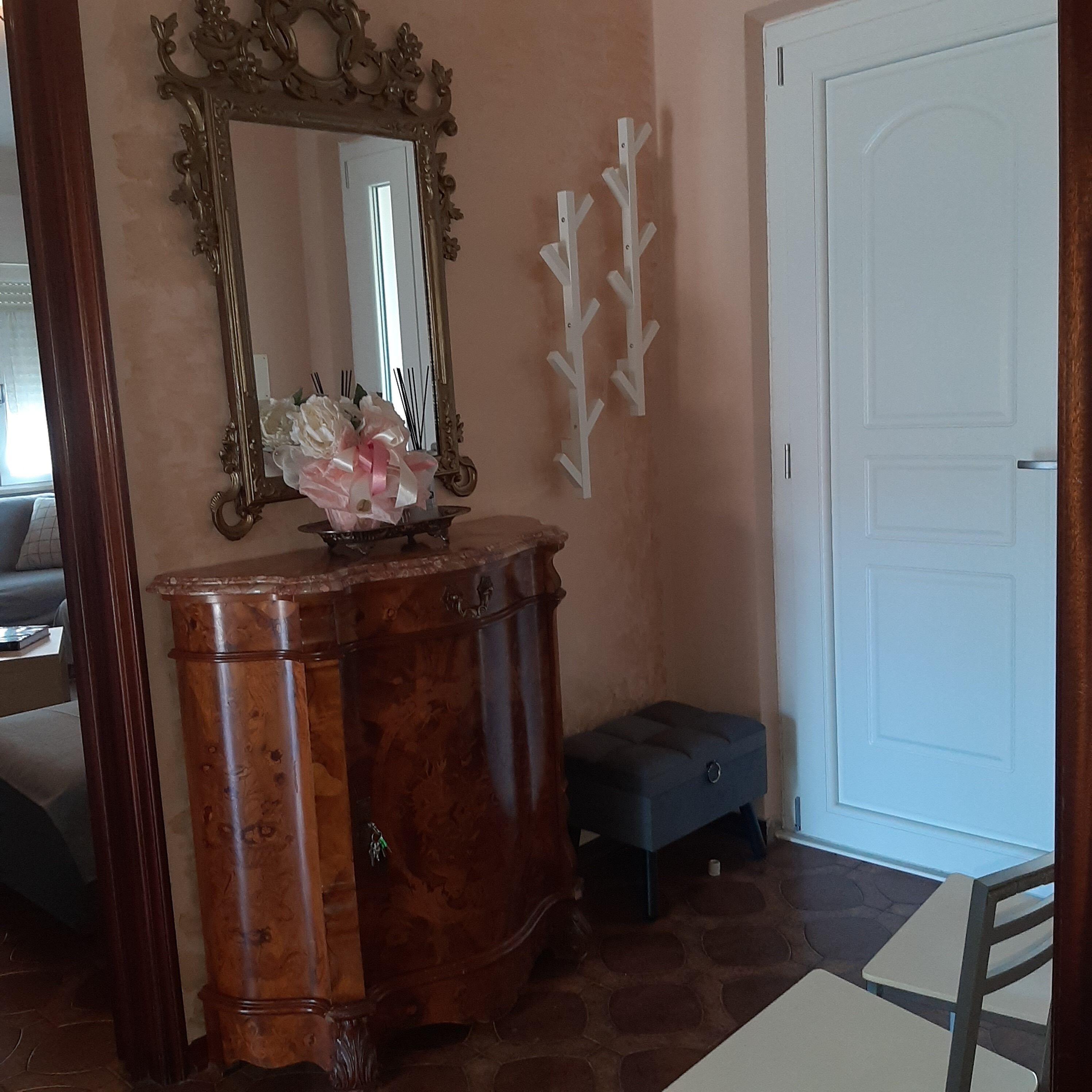 A wooden console table with a mirror and a vase of flowers, a white door, and a small bench.