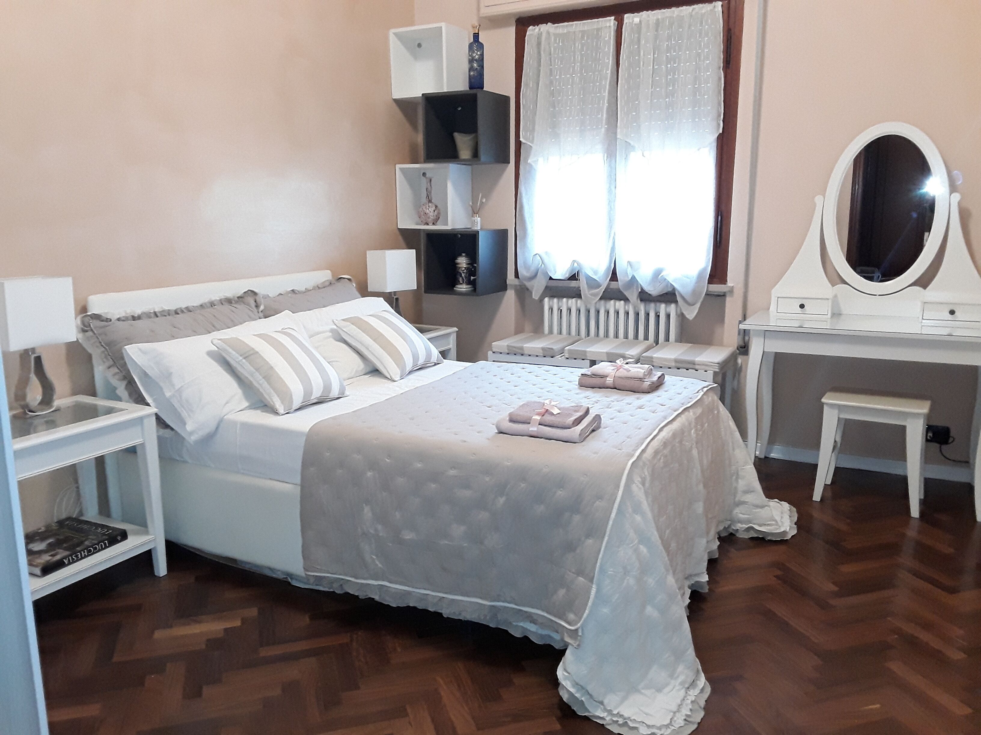 A neatly arranged bedroom with a bed, bedside tables, a vanity with a mirror, and a radiator.