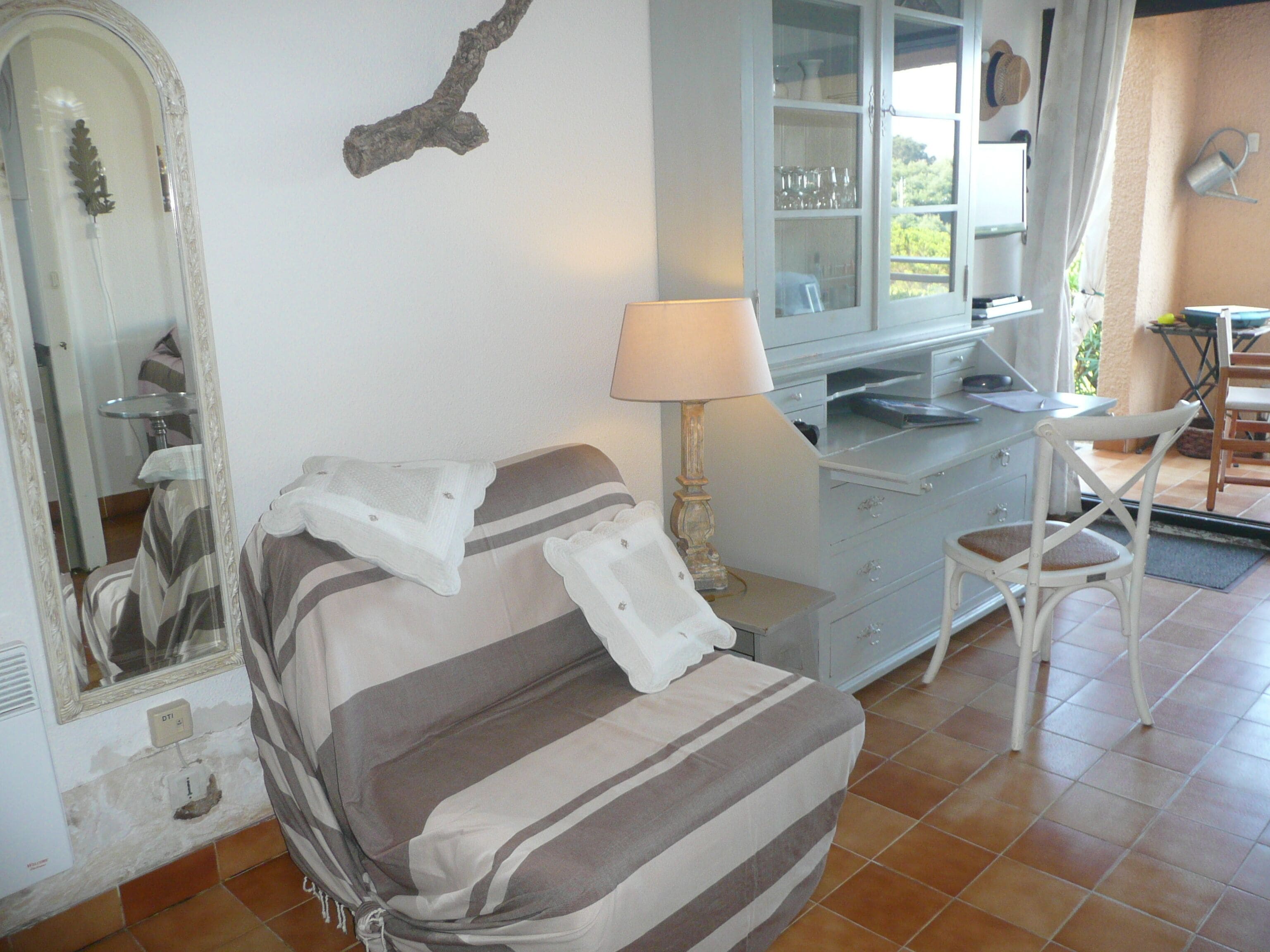 Une pièce avec un canapé à rayures, une lampe, un miroir et un coin repas comprenant des chaises et une table.