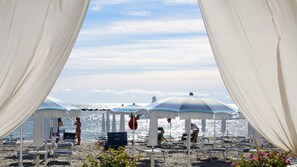 A beach with white canopies and sun loungers, a clear sky, and the ocean in the background.