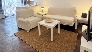 Un soggiorno con divano, tavolino, tappeto, televisore e cucina sullo sfondo.