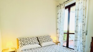 Una camera da letto con un letto, un comodino, una finestra con tende e un asciugamano sul letto.