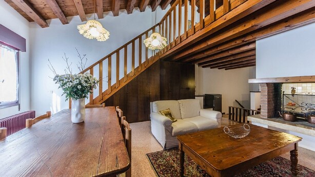 A spacious living room with a wooden staircase, a fireplace, and a dining area with a large wooden table and chairs. - Novalesi House (only 20 minutes to Venice) (Noale)