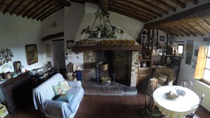 Een rustiek interieur met een stenen openhaard, houten balken, een bank en een eettafel.