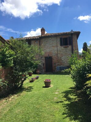 A stone building with a tiled roof, a chimney, and a door. There are potted plants and a well-maintained lawn in front.