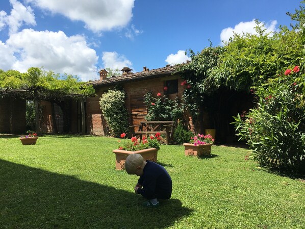 A child playing in a well-maintained garden with a rustic building in the background.