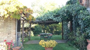 Een tuin met een bakstenen muur, een houten pergola en planten in potten.