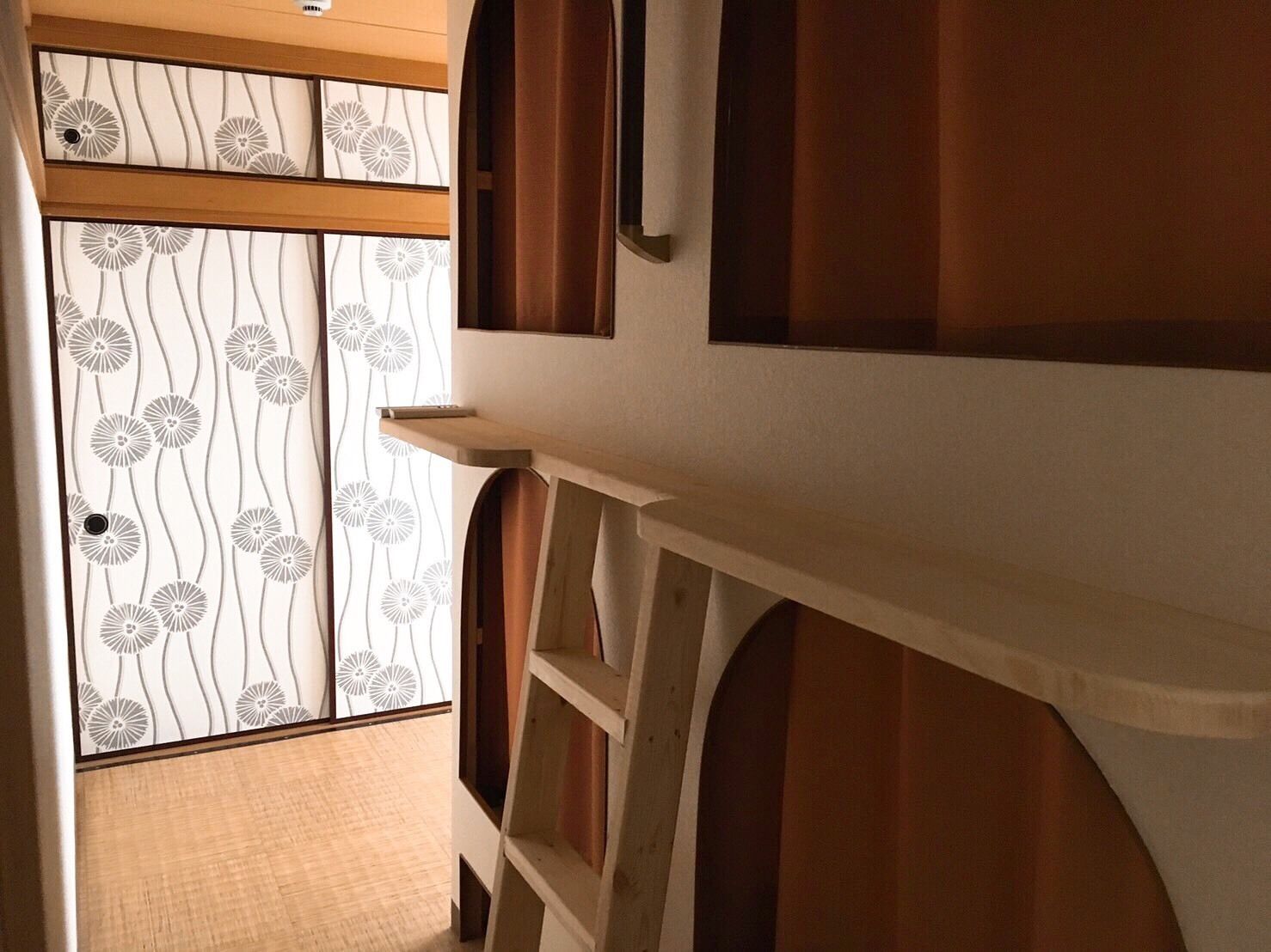 A hallway with a wooden floor, a sliding door with a floral pattern, and a white wall with a shelf.